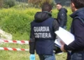 Agenti della Guardia Costiera in giubbotto operativo ispezionano un'area recintata con nastro bianco-rosso in aperta campagna