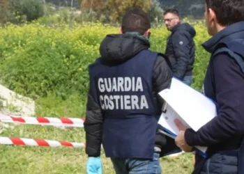 Agenti della Guardia Costiera in giubbotto operativo ispezionano un'area recintata con nastro bianco-rosso in aperta campagna