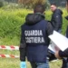 Agenti della Guardia Costiera in giubbotto operativo ispezionano un'area recintata con nastro bianco-rosso in aperta campagna