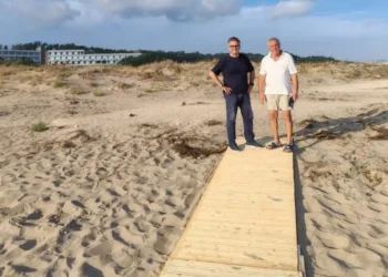 Due uomini in piedi sulla nuova passerella in legno sulla spiaggia di Passo Marinaro, con le dune e un edificio sullo sfondo