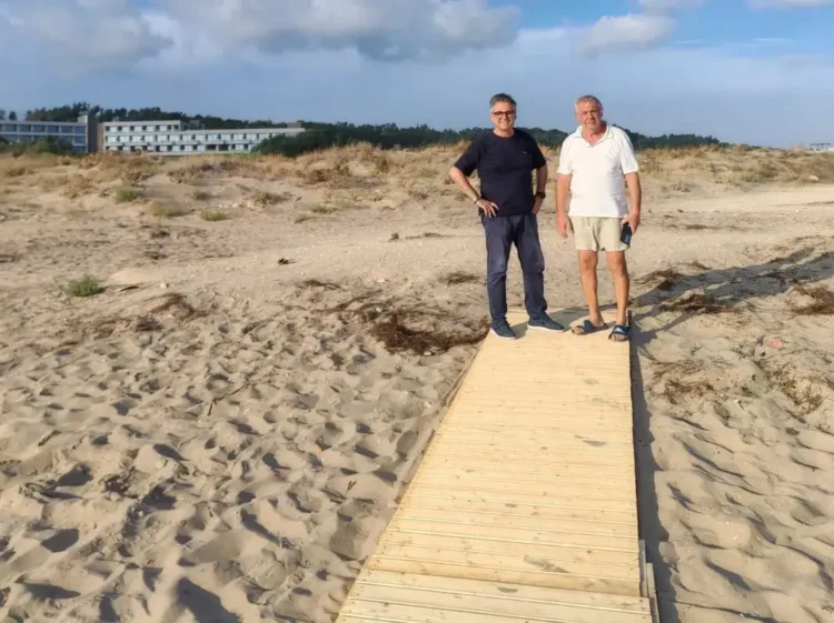 Due uomini in piedi sulla nuova passerella in legno sulla spiaggia di Passo Marinaro, con le dune e un edificio sullo sfondo