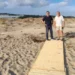 Due uomini in piedi sulla nuova passerella in legno sulla spiaggia di Passo Marinaro, con le dune e un edificio sullo sfondo