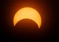 Eclissi solare parziale: la Luna copre la parte inferiore del disco solare, che appare arancione su sfondo scuro.