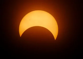 Eclissi solare parziale: la Luna copre la parte inferiore del disco solare, che appare arancione su sfondo scuro.