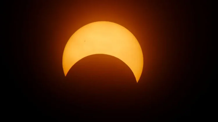 Eclissi solare parziale: la Luna copre la parte inferiore del disco solare, che appare arancione su sfondo scuro.