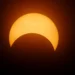 Eclissi solare parziale: la Luna copre la parte inferiore del disco solare, che appare arancione su sfondo scuro.