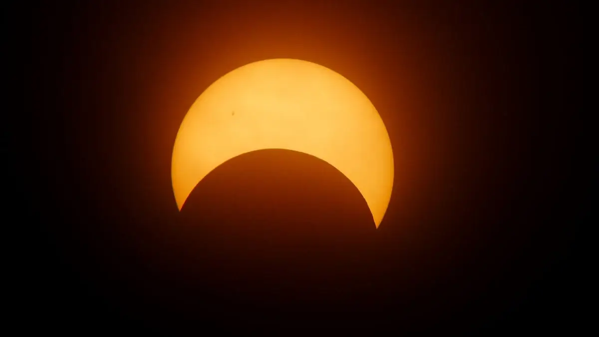 Eclissi solare parziale: la Luna copre la parte inferiore del disco solare, che appare arancione su sfondo scuro.