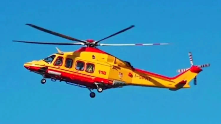 Elicottero del 118 in volo su cielo azzurro, livrea giallo-rossa, impegnato in un intervento di soccorso sanitario.