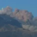 Colonna di cenere grigia si alza dal cratere dell'Etna su cielo sereno, con neve residua sul versante
