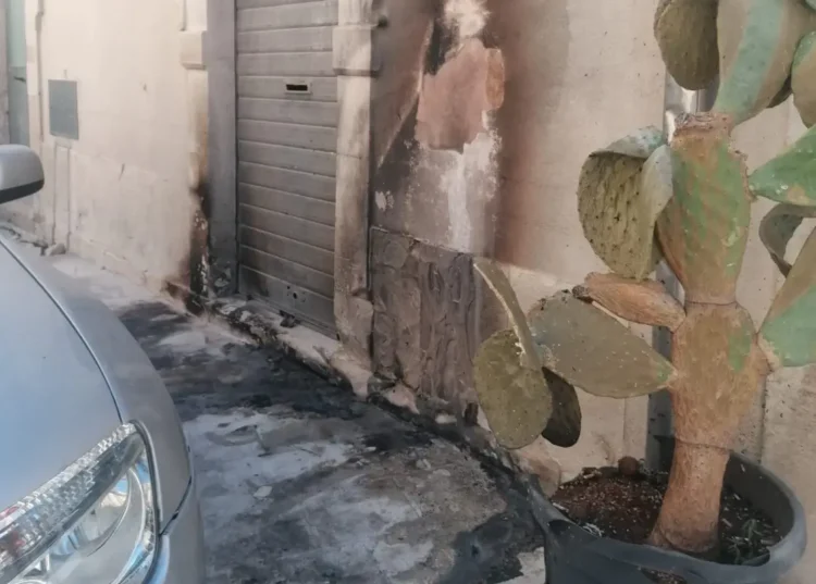 Facciata di un edificio storico annerita dal fumo con intonaco scrostato e suolo bruciacchiato dopo l'incendio di un mastello