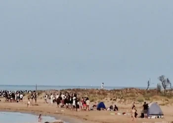 Decine di giovani sulla spiaggia di Playa Grande a Scicli al mattino, con tende ancora montate sulla battigia