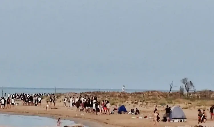 Decine di giovani sulla spiaggia di Playa Grande a Scicli al mattino, con tende ancora montate sulla battigia