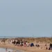 Decine di giovani sulla spiaggia di Playa Grande a Scicli al mattino, con tende ancora montate sulla battigia