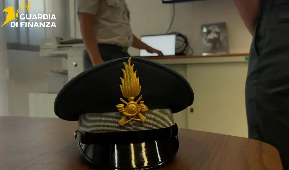 Berretto con fregio dorato della Guardia di Finanza su scrivania, militare in uniforme sullo sfondo