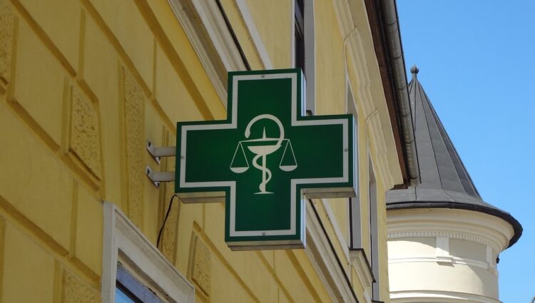 Insegna verde di una farmacia con il simbolo del mortaio e del serpente, su una parete gialla d'angolo.