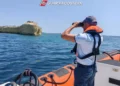 Militare della Guardia Costiera osserva il mare con il binocolo a bordo di un gommone, vicino a una costa rocciosa