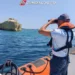 Militare della Guardia Costiera osserva il mare con il binocolo a bordo di un gommone, vicino a una costa rocciosa