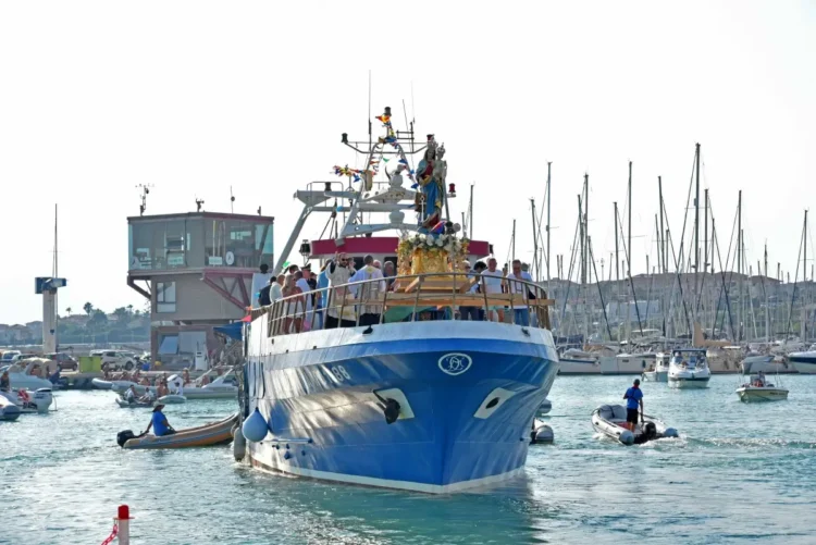 Il simulacro di Santa Maria di Portosalvo trasportato su un peschereccio blu nel porto di Marina di Ragusa, circondato da piccole imbarcazioni