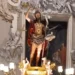 Statua di San Giovanni Battista nella nicchia dorata della cattedrale di Ragusa, con candelabri accesi alla base