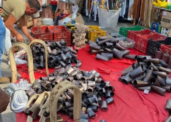 Bancarella con campanacci in metallo, finimenti in legno e cinghie di cuoio su un telo rosso al mercato