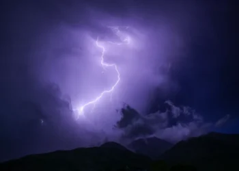 Un fulmine illumina il cielo notturno sopra il profilo scuro di una catena montuosa