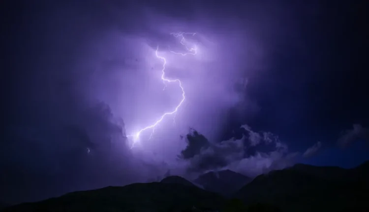 Un fulmine illumina il cielo notturno sopra il profilo scuro di una catena montuosa