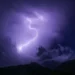 Un fulmine illumina il cielo notturno sopra il profilo scuro di una catena montuosa