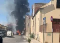 Colonna di fumo nero e fiamme in via Iannizzotto a Vittoria, furgone bianco in primo piano e passanti sul posto.