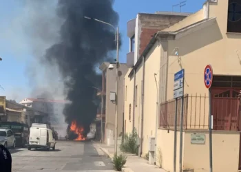 Colonna di fumo nero e fiamme in via Iannizzotto a Vittoria, furgone bianco in primo piano e passanti sul posto.
