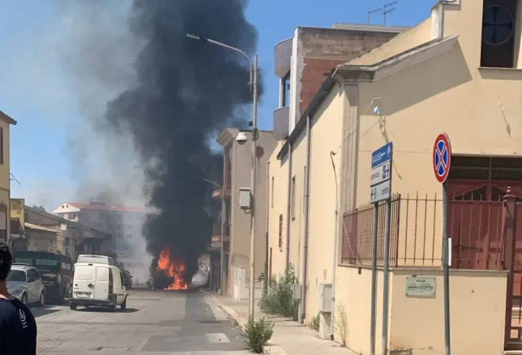 Colonna di fumo nero e fiamme in via Iannizzotto a Vittoria, furgone bianco in primo piano e passanti sul posto.
