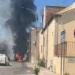 Colonna di fumo nero e fiamme in via Iannizzotto a Vittoria, furgone bianco in primo piano e passanti sul posto.