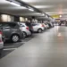 Auto parcheggiate in un parcheggio multipiano coperto, con corsia centrale e posti auto su entrambi i lati.