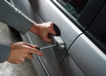 Mani con un cacciavite forzano la serratura dello sportello di un'auto in sosta.