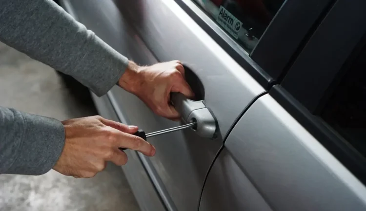 Mani con un cacciavite forzano la serratura dello sportello di un'auto in sosta.
