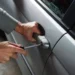 Mani con un cacciavite forzano la serratura dello sportello di un'auto in sosta.
