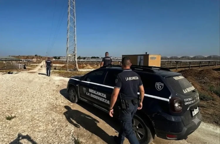 Due guardie giurate dell'istituto La Sicurezza ispezionano una stradina sterrata accanto a un parco fotovoltaico in aperta campagna.