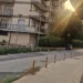 Una via residenziale di Modica con marciapiede, dissuasori e cassonetti per la raccolta differenziata, al tramonto