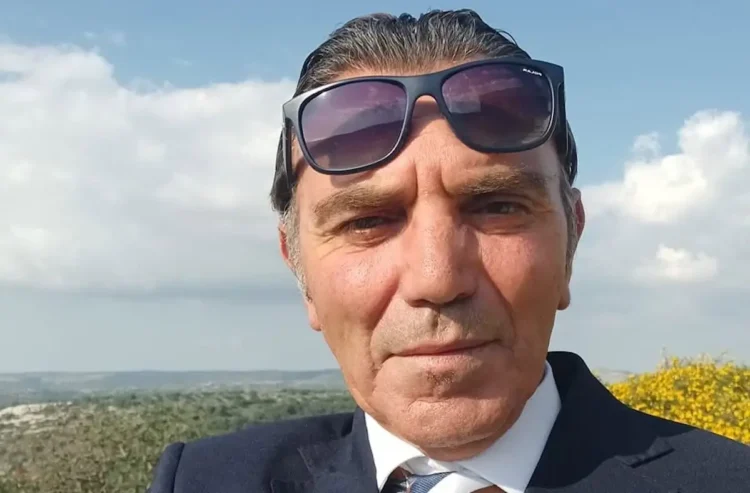 Giuseppe Damasco in un primo piano, giacca scura e camicia bianca, sullo sfondo cielo e vegetazione.