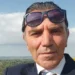 Giuseppe Damasco in un primo piano, giacca scura e camicia bianca, sullo sfondo cielo e vegetazione.