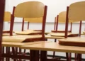 Banchi e sedie di legno vuoti in un'aula scolastica, ripresi in prospettiva con luce naturale.