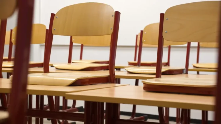 Banchi e sedie di legno vuoti in un'aula scolastica, ripresi in prospettiva con luce naturale.
