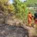 Squadre antincendio in tuta arancione osservano un'area boschiva bruciata su un versante collinare