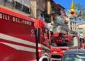 Tre automezzi dei Vigili del Fuoco in strada davanti a un edificio con segni di bruciatura sul balcone al secondo piano