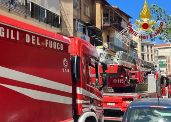 Tre automezzi dei Vigili del Fuoco in strada davanti a un edificio con segni di bruciatura sul balcone al secondo piano