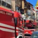 Tre automezzi dei Vigili del Fuoco in strada davanti a un edificio con segni di bruciatura sul balcone al secondo piano