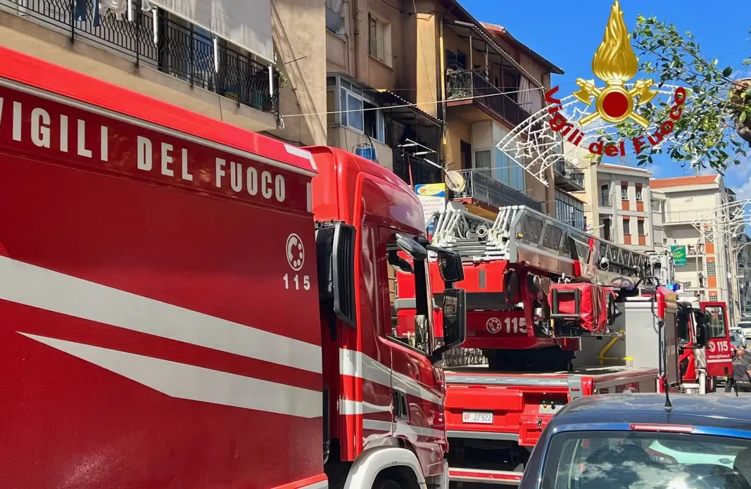 Tre automezzi dei Vigili del Fuoco in strada davanti a un edificio con segni di bruciatura sul balcone al secondo piano