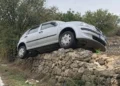 Auto sospesa su un muro a secco accanto a una strada rurale, dopo essere uscita dalla carreggiata.