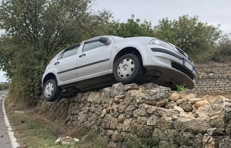 Auto sospesa su un muro a secco accanto a una strada rurale, dopo essere uscita dalla carreggiata.