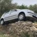 Auto sospesa su un muro a secco accanto a una strada rurale, dopo essere uscita dalla carreggiata.