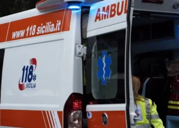 Ambulanza del 118 Sicilia con portiere posteriori aperte e operatrice sanitaria in giubbotto giallo fluorescente.